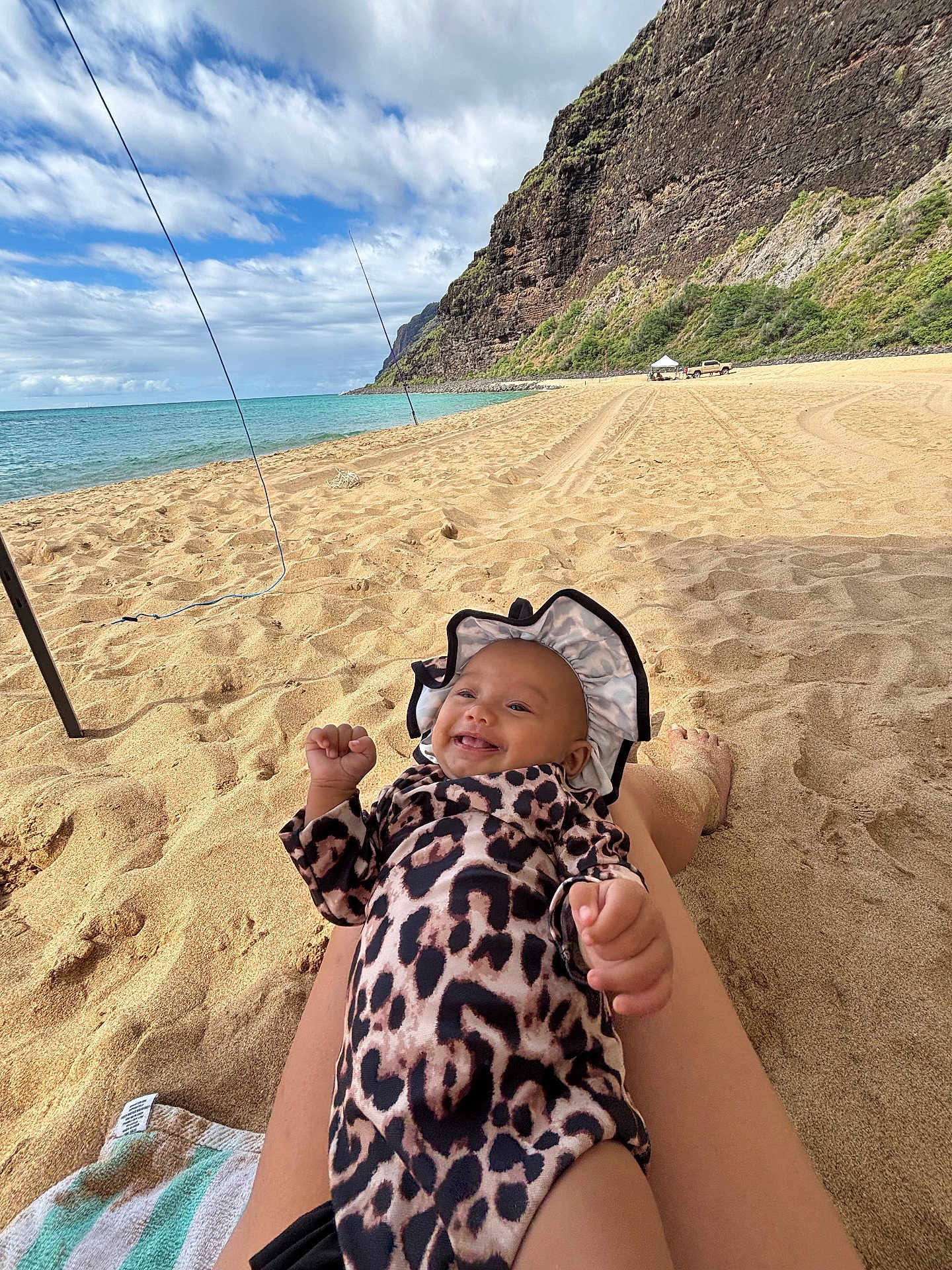 Mailehea is registered to the contest to win money with this photo: baby, beach, cliffs, clouds, happy, hat, infant, legs, leopard_print, nature, ocean, outdoor, relaxing, sand, sky, smiling, sunshine, towel, vacation, water