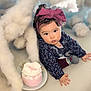 baby, blue_background, bow, cake, child, clothing, clouds, crawling, curious, fluffy, headband, indoors, long_sleeves, pink, plate, portrait, sock, soft_surface, toddler, white