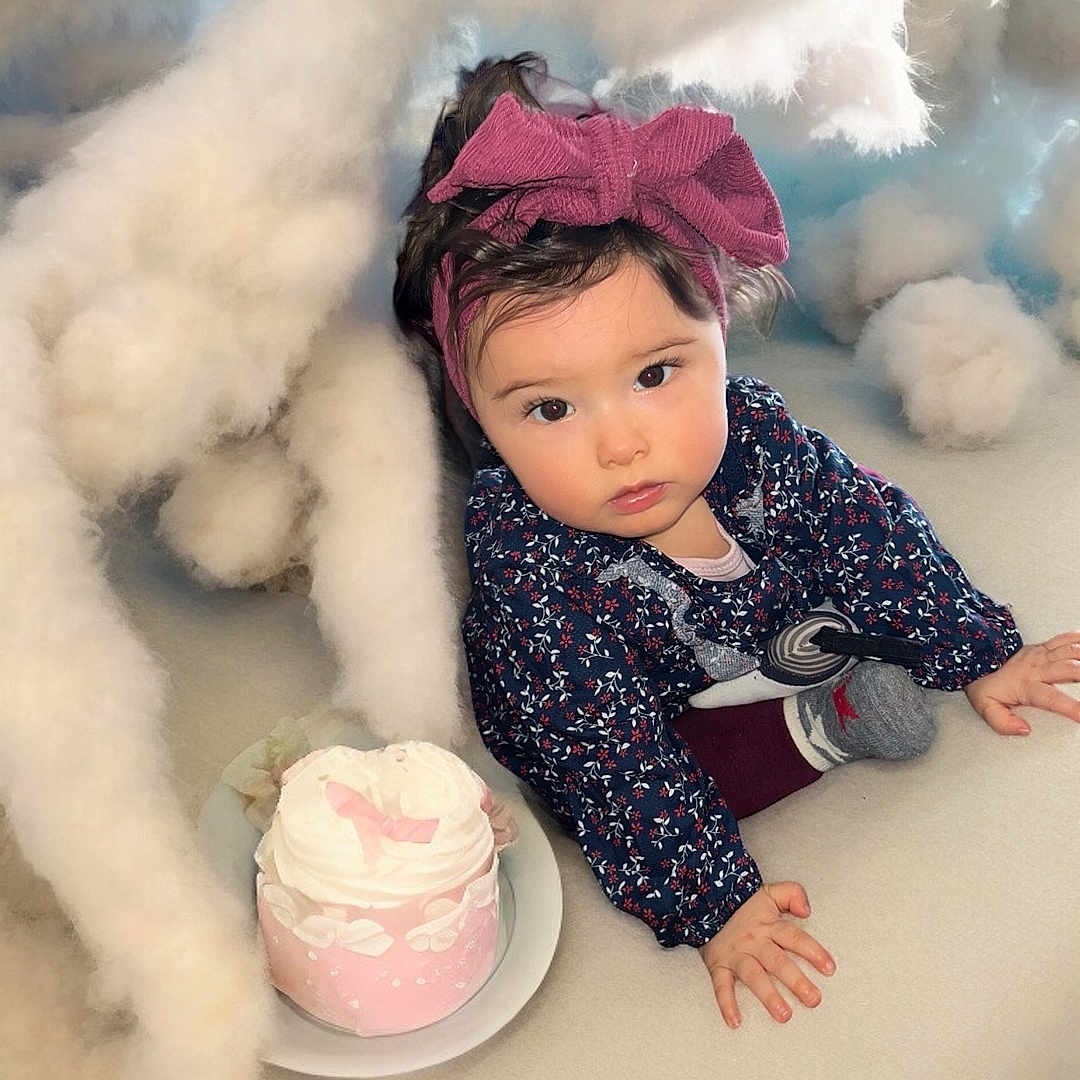 Sibel a rejoint le concours — aidez-le/la à gagner de superbes lots ! baby, blue_background, bow, cake, child, clothing, clouds, crawling, curious, fluffy, headband, indoors, long_sleeves, pink, plate, portrait, sock, soft_surface, toddler, white