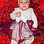 baby, infant, child, dress, headband, bow, tutu, red_background, fabric, blanket, lying_down, portrait, wide_eyes, white_clothing, tights, shoes, cute, satin, hand, face