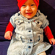 Ayline participe au concours pour gagner de l'argent avec cette photo : baby, infant, child, red_turban, headwrap, denim_dress, smiling, sitting, sofa, navy_background, white_tights, hands, eyes, portrait, cute, indoor, clothing, button, happy, fashion