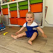 Eden participe au concours pour gagner de l'argent avec cette photo : toddler, child, smiling, sitting, playroom, toys, storage_bins, colorful, wooden_floor, overalls, white_shirt, happy, indoor, face, blue_eyes, plastic_toys, whisk, floor, person, young_child