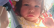 Luna is registered to the contest to win money with this photo: child, toddler, hat, yellow_dress, stroller, sunlight, hand, face, outdoor, expression, waving, fabric, bow, cute, person, summer, shade, closeup, young_child, casual