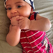 Yazeed joined the competition — help win amazing prizes! baby, infant, child, face, hand, headwear, clothing, red_stripes, lying_down, cute, skin, chewing, curious, closeup, portrait, soft_surface, indoors, baby_garment, expression, young