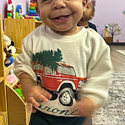 Syair is registered to the contest to win money with this photo: toddler, child, smiling, indoor, playroom, toys, clothing, sweater, pants, car_print, happy, motion_blur, person, floor, rug, wood_floor, furniture, background, young_child, cute