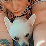 person, dog, white_dog, close_up, selfie, tattoo, leopard_print, blanket, indoor, cute, pet, animal, face, eyes, expression, cuddle, resting, soft_texture, cozy, warm_lighting