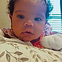 baby, child, infant, curly_hair, hair_clip, pillow, floral_pattern, close_up, face, eyes, expression, indoor, natural_light, resting, cute, adorable, person, soft_lighting, curiosity, young