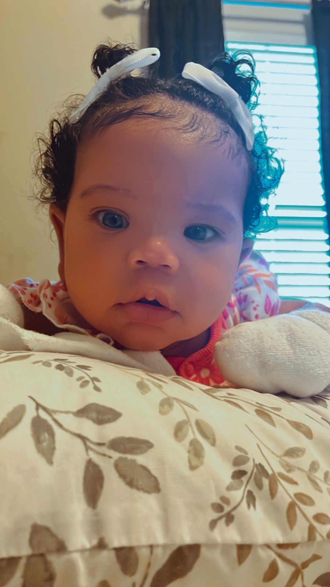 Jaci is registered to the contest to win money with this photo: baby, child, infant, curly_hair, hair_clip, pillow, floral_pattern, close_up, face, eyes, expression, indoor, natural_light, resting, cute, adorable, person, soft_lighting, curiosity, young