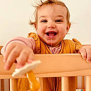 Victoire participe au concours pour gagner de l'argent avec cette photo : toddler, child, baby, smiling, drool, pacifier, crib, wooden_crib, clothing, indoor, happy, face, hand, hair, person, portrait, toy, infant, cute, playful