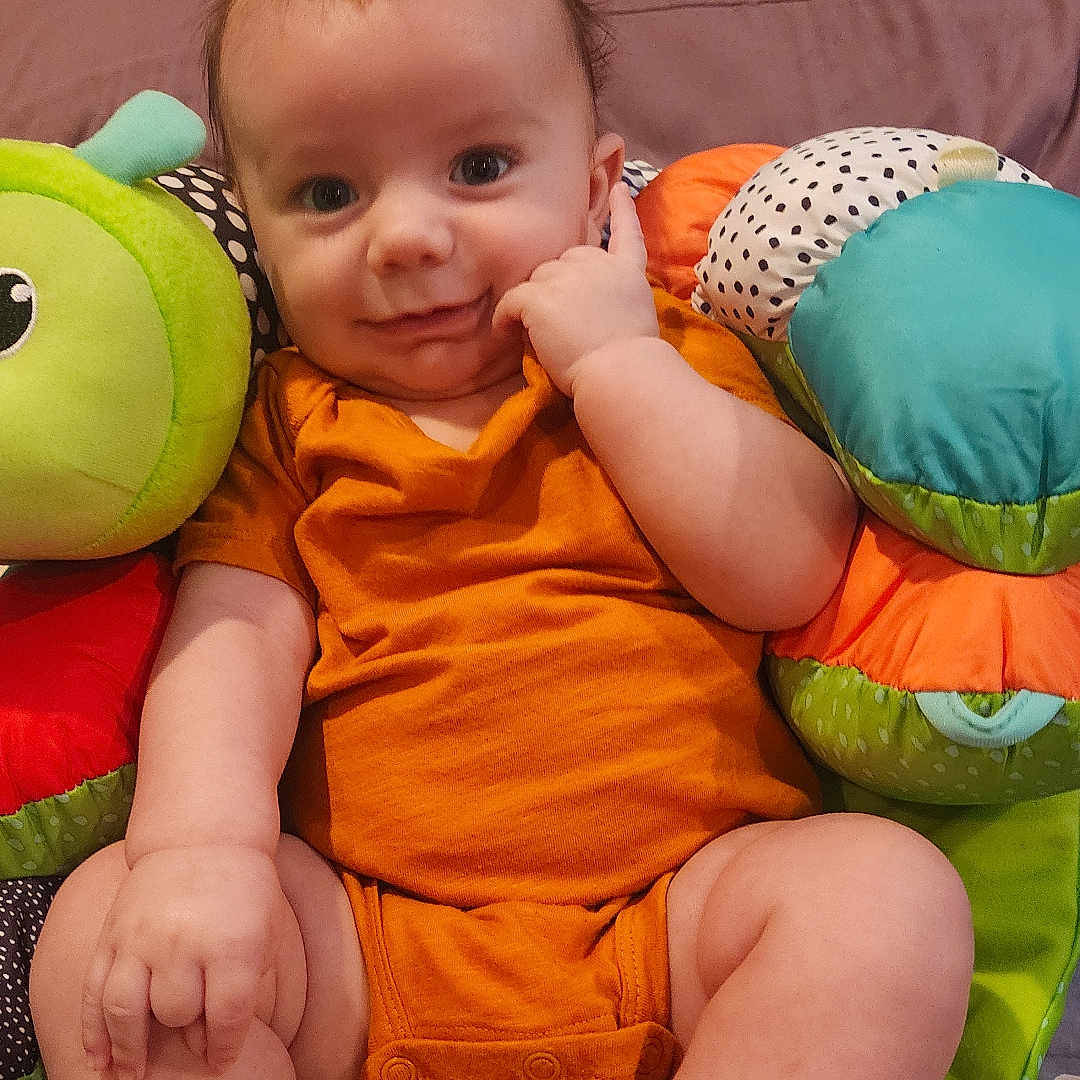 R.j is registered to the contest to win money with this photo: baby, blanket, bodypart, couch, cushion, face, finger, furniture, hand, happy, head, homedecor, linen, person, photography, pillow, portrait, sitting, smile, toy