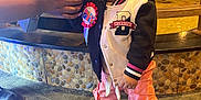 Khalyla joined the competition — help win amazing prizes! toddler, child, indoor, person, standing, holding_hand, jacket, pants, sneakers, hair_accessories, birthday_badge, carpet, stone_wall, adult_hand, fashion, cute, young_child, portrait, celebration, smiling