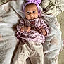 baby, infant, blanket, heart_pattern, headband, purple, pink_clothing, long_sleeve, pants, soft_texture, lying_down, indoors, curious_expression, small_hands, cute, cozy, sleepwear, person, portrait, child