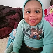 Koda joined the competition — help win amazing prizes! baby, child, smiling, hoodie, indoor, blanket, cushion, happy, person, cute, portrait, seated, clothing, face, young_child, cozy, warm, infant, casual, home