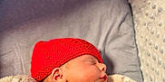 George is registered to the contest to win money with this photo: baby, baby_bed, blanket, child, comfort, cozy, cushion, cute, face, indoor, infant, knitted, newborn, peaceful, portrait, red_hat, resting, sleeping, soft_texture, warm