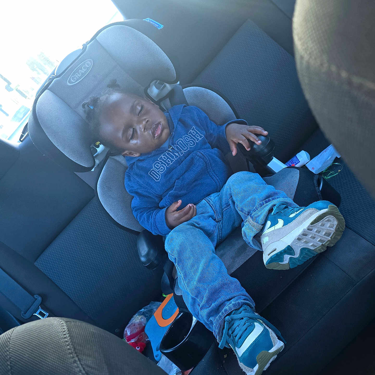 J'Ron is registered to the contest to win money with this photo: backseat, blue_hoodie, car_interior, car_seat, child, clothing, container, footwear, hair_buns, jeans, peaceful, seat, seatbelt, sleeping, sneakers, sunlight, toddler, toy, window, young_child