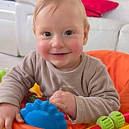 Jimmy a rejoint le concours — aidez-le/la à gagner de superbes lots ! baby, child, toy, indoor, smiling, happy, face, hands, colorful, play, infant, young_child, person, closeup, couch, furniture, red, orange, blue, green