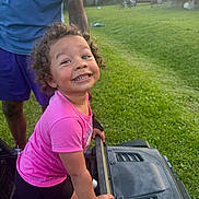 Lillyana joined the competition — help win amazing prizes! adult, backyard, black_shorts, casual_clothing, child, curly_hair, daylight, fun, grass, greenery, happy, outdoor, person, pink_shirt, play, smile, sunlight, toddler, toy_car, vehicle