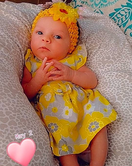 Carolyn is registered to the contest to win money with this photo: baby, baby_toddler_clothing, child, hair_accessory, headwear, pattern, person, pink, product, skin, smile, textile, toddler, toy, yellow