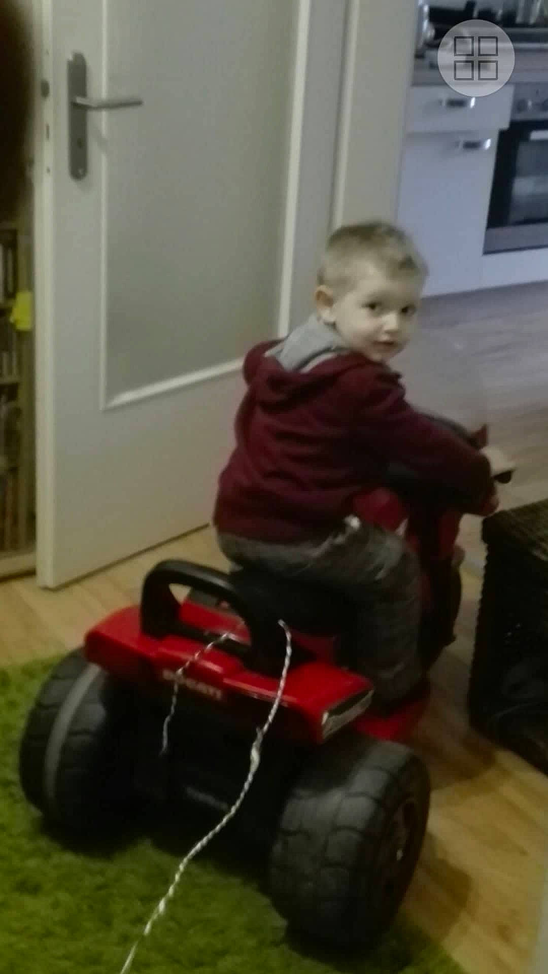 Timothy is registered to the contest to win money with this photo: automotive_tire, automotive_wheel_system, child, door, flooring, fun, hardwood, lawn_mower, motor_vehicle, mower, person, play, riding_toy, room, sitting, tire, toddler, tread, vehicle, wheel
