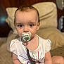 Elora is registered to the contest to win money with this photo: baby, blurred_background, child, closeup, clothing, couch, cute, expression, face, furniture, hand, indoor, pacifier, pacifier_clip, person, portrait, sitting, toddler, white_shirt, young_child