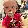 bed, blanket, child, clothing, curious, expression, eyes, face, furniture, hair, hand, indoor, minnie_mouse, pacifier, person, red_shirt, room, toddler, toy, young_child