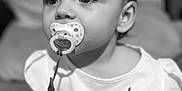 Elora joined the competition — help win amazing prizes! baby, black_and_white, child, closeup, clothing, couch, cushion, cute, expression, eyes, face, hand, indoors, infant, pacifier, person, portrait, shirt, sitting, young