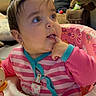 baby, child, infant, sitting, activity_seat, pink_clothing, striped_shirt, curious, face, eyes, finger, hand, indoor, home, furniture, chair, toy, colorful, portrait, happy
