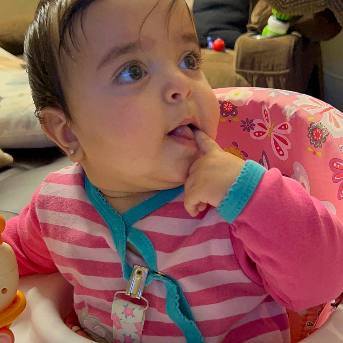Lara joined the competition — help win amazing prizes! baby, child, infant, sitting, activity_seat, pink_clothing, striped_shirt, curious, face, eyes, finger, hand, indoor, home, furniture, chair, toy, colorful, portrait, happy