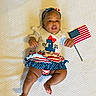 Anika joined the competition — help win amazing prizes! 4th_of_july, american_flag, baby, blanket, celebration, child, clothing, cute, festive, happy, headband, holiday, infant, lying_down, one_year_old, person, portrait, red_white_blue, smiling, toddler