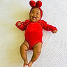 Anika is registered to the contest to win money with this photo: adorable, baby, baby_arms, baby_legs, blanket, bunny_ears, cheerful, child, closeup, cute, happy, headwear, indoor, infant, lying_down, one_person, portrait, red_outfit, smiling, soft_texture