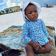 Rowyn is registered to the contest to win money with this photo: beach, blanket, buildings, child, clouds, cute, daytime, hat, outdoor, relaxing, sand, sitting, sky, summer, sunhat, swimsuit, toddler, vacation, waterfront, young_child