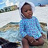 beach, blanket, buildings, child, clouds, cute, daytime, hat, outdoor, relaxing, sand, sitting, sky, summer, sunhat, swimsuit, toddler, vacation, waterfront, young_child