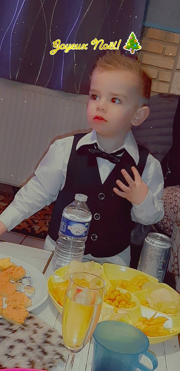 Julian participe au concours pour gagner de l'argent avec cette photo : bottle, bow_tie, chair, child, cooking, dress_shirt, drink, drinkware, food, formal_wear, junk_food, person, plastic_bottle, plate, suit, table, tableware, tie, toddler, water_bottle