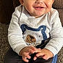 baby, child, smiling, sitting, sweater, bear_design, pants, white_sneakers, carpet, cushion, hands, face, indoor, cute, happy, portrait, clothing, infant, young_child, cozy