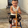 toddler, child, smiling, wooden_toy, rocking_horse, indoor, floor, camo_pants, white_tank_top, barefoot, happy, playtime, toy, furniture, person, portrait, cute, young_child, hands, face
