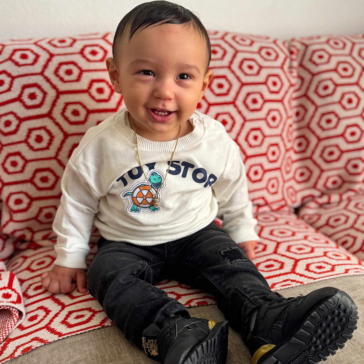 Oziel joined the competition — help win amazing prizes! black_pants, blanket, boots, child, clothing, couch, cute, face, happy, home, indoor, jewelry, patterned, person, portrait, seated, smiling, sweater, toddler, young_child