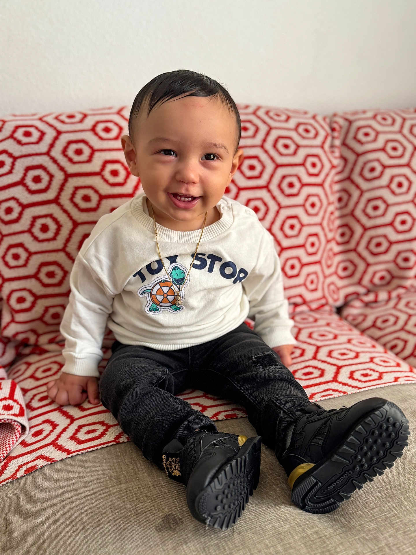 Oziel joined the competition — help win amazing prizes! toddler, child, smiling, indoor, couch, blanket, patterned, clothing, boots, sweater, face, happy, portrait, person, seated, young_child, jewelry, black_pants, home, cute