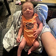 Maverick joined the competition — help win amazing prizes! newborn, baby, infant, sleeping, orange_onesie, towel, arm, hand, table, pen, floor, carpet, person, indoor, cozy, clothing, resting, cute, peaceful, home