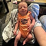 newborn, baby, infant, sleeping, orange_onesie, towel, arm, hand, table, pen, floor, carpet, person, indoor, cozy, clothing, resting, cute, peaceful, home