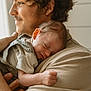 baby, adult, curly_hair, sleeping, shoulder, close_up, indoor, natural_light, portrait, smiling, person, skin, clothing, hand, family, love, affection, gentle, comfort, warm