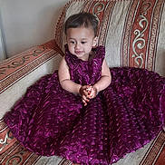 Zehak is registered to the contest to win money with this photo: toddler, child, purple_dress, sofa, patterned_sofa, henna, clothing, indoor, sitting, curious, small_child, furniture, decor, floor, wooden_floor, cute, portrait, person, young_child, smiling