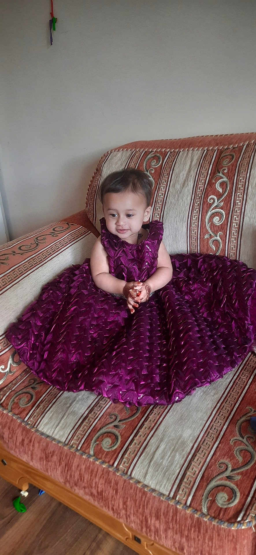 Zehak is registered to the contest to win money with this photo: toddler, child, purple_dress, sofa, patterned_sofa, henna, clothing, indoor, sitting, curious, small_child, furniture, decor, floor, wooden_floor, cute, portrait, person, young_child, smiling