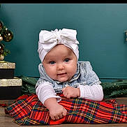 Savanna participe au concours pour gagner de l'argent avec cette photo : baby, infant, child, white_bow, denim_jacket, plaid_blanket, christmas_tree, gold_baubles, presents, holiday_decor, teal_wall, floor, wooden_floor, posing, cute, portrait, smiling, indoor, festive, cozy