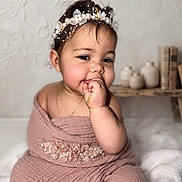 Emily joined the competition — help win amazing prizes! baby, child, portrait, headband, pearl, flower, pink_cloth, textured_fabric, hand_in_mouth, smiling, face, indoor, decor, vase, books, bench, cute, infant, person, soft_lighting