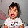 toddler, child, smiling, happy, shirt, text, indoor, portrait, baby, necklace, cute, funny_expression, hair, pink, white, wall_decor, sitting, person, clothing, celebration