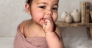 Emily joined the competition — help win amazing prizes! baby, child, portrait, headband, pearl, flower, blanket, pink, cute, chubby_cheeks, hand, sucking_fingers, soft_lighting, indoor, decor, books, vases, expression, wrapped, sitting