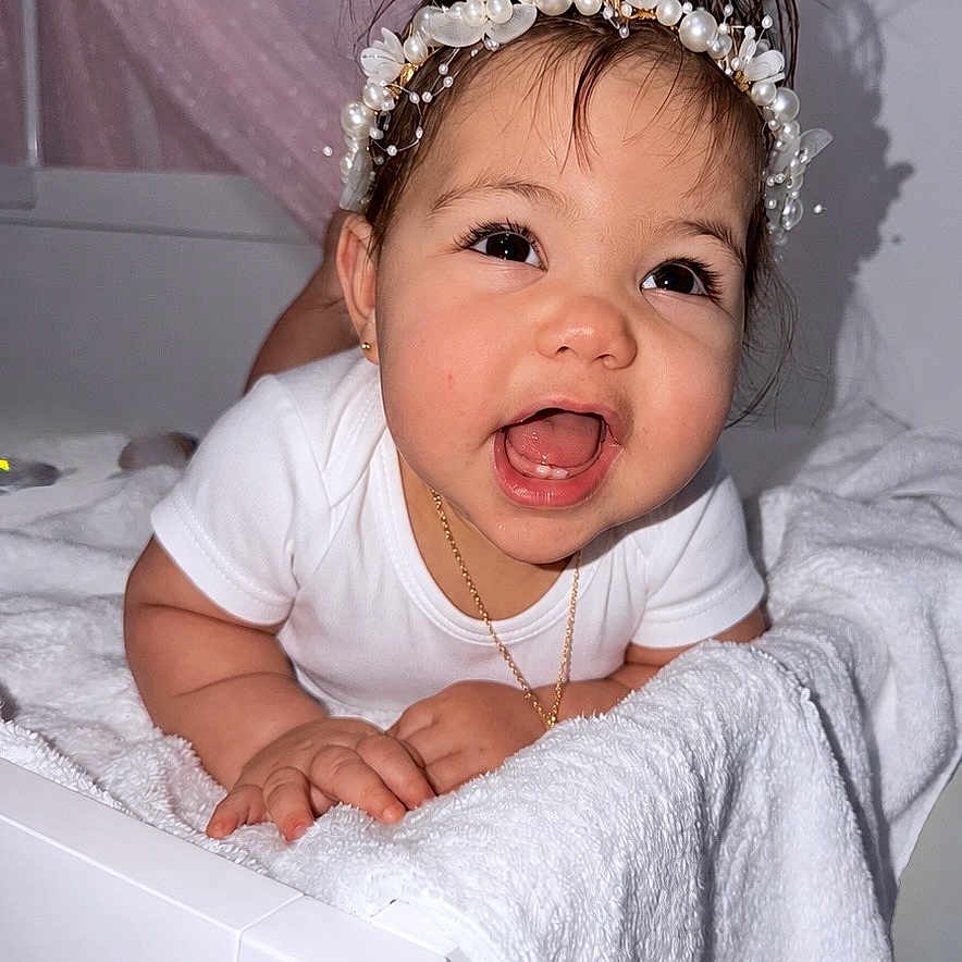 Emily joined the competition — help win amazing prizes! baby, child, toddler, headband, pearl, flower, white_clothing, smiling, happy, towel, bed, indoor, person, cute, portrait, face, skin, hand, decor, star