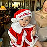 baby, child, christmas_hat, red_clothing, white_fur, holiday, festive, smiling, woman, indoor, living_room, carpet, lamp, furniture, portrait, cute, holding, happy, celebration, family