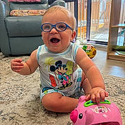 Jackson joined the competition — help win amazing prizes! baby, child, glasses, mickey_mouse, toy, pink_piggy_bank, carpet, living_room, recliner_chair, baby_gate, ball, smiling, sitting, playful, indoor, cute, happy, shorts, sleeveless_shirt, floor