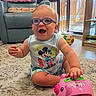 baby, child, glasses, mickey_mouse, toy, pink_piggy_bank, carpet, living_room, recliner_chair, baby_gate, ball, smiling, sitting, playful, indoor, cute, happy, shorts, sleeveless_shirt, floor